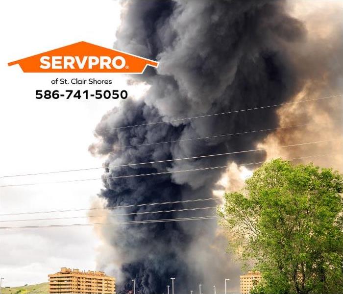 A large plume of smoke fills the air above a commercial building on fire.